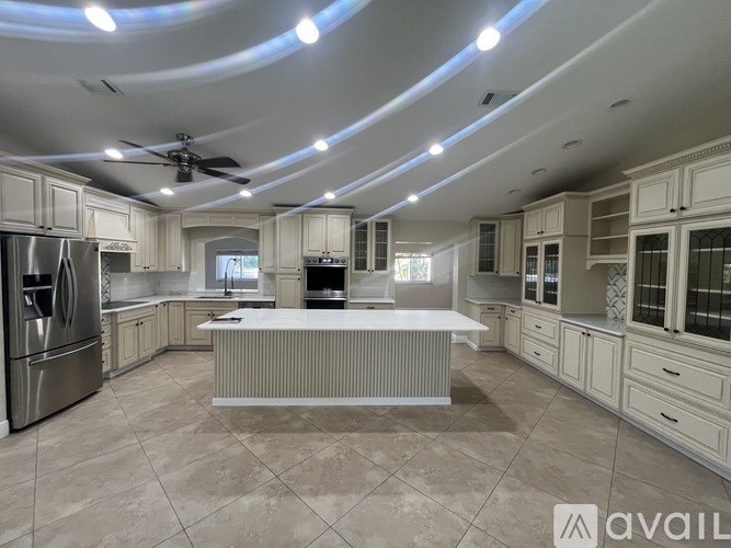 A spacious kitchen with a central island and a refrigerator on the left.