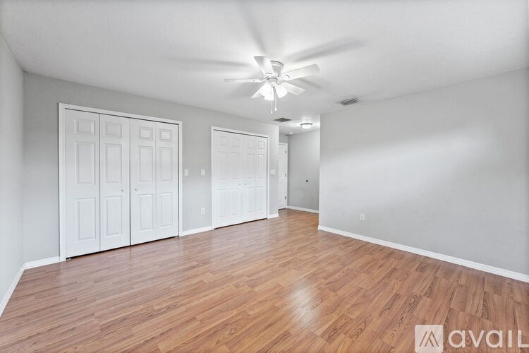 A room with wooden floors and white walls, featuring a ceiling fan and two doors.