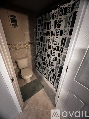 A bathroom with a toilet, a shower curtain, and a mat on the floor.