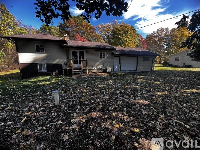A house with a brown roof and a white garage door is surrounded by fallen leaves.