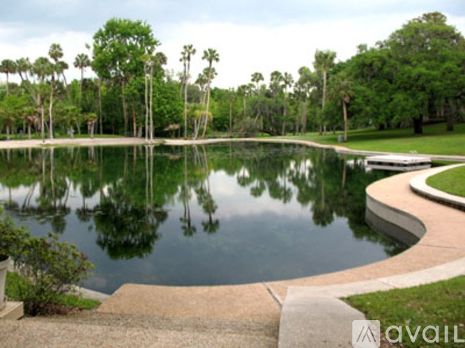 A calm pond surrounded by trees and a concrete walkway.