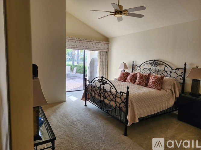A bedroom with a bed, a ceiling fan, and a window with a view of the outside.