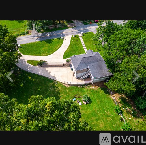 A house with a grey roof is surrounded by a green lawn and trees.