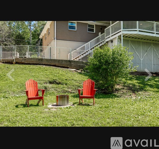 Two red chairs are placed on a lawn in front of a house.