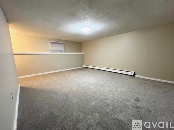 A spacious room with a carpeted floor and a window with blinds.