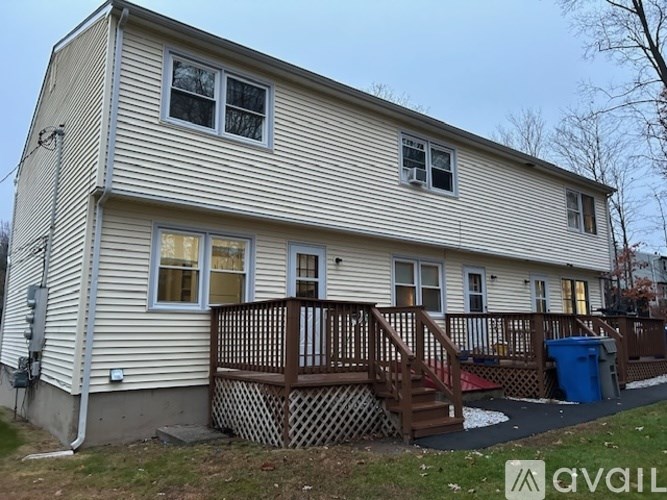 A two-story house with a deck and a blue trash can.