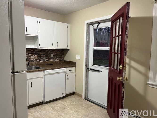 A kitchen with white cabinets and a red door.