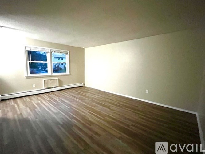 A room with wooden flooring and a window showing a view of trees and a house.