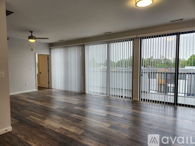 A spacious room with wooden flooring and large windows.
