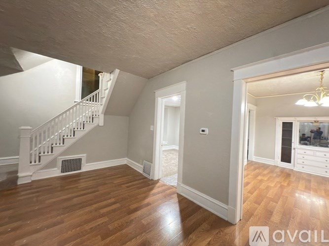 A spacious room with wooden floors and a staircase leading to another level.