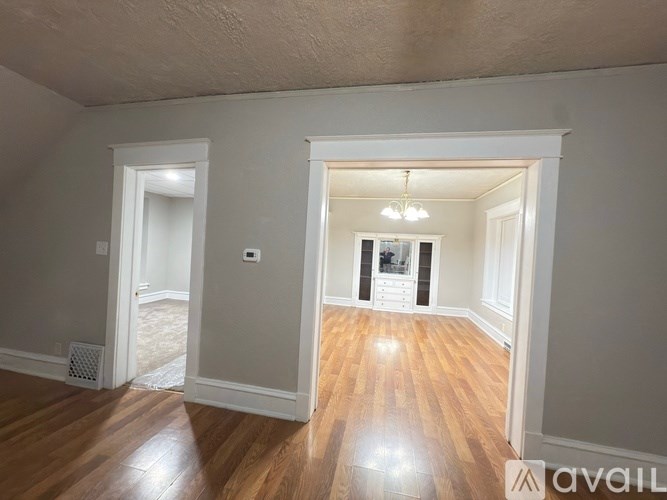 A room with wooden floors and white walls, with a doorway leading to another room.