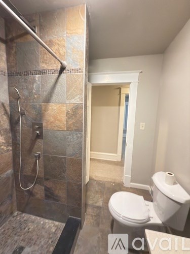 A bathroom with a toilet, a walk in shower and a doorway leading to another room.
