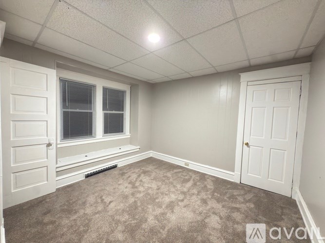 A room with a carpeted floor, two doors, and a window with blinds.