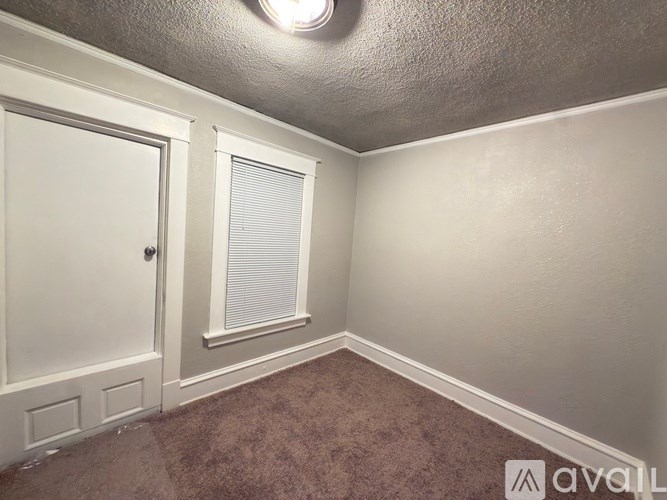 A room with a carpeted floor, a door, and a window with blinds.