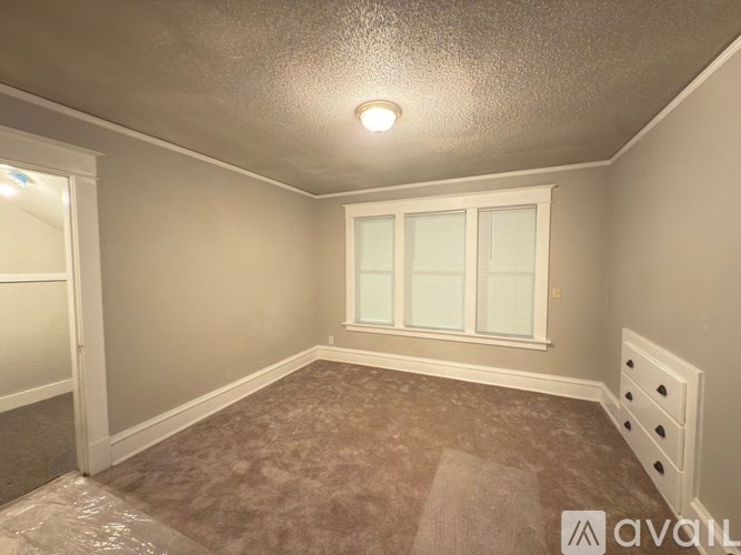 A room with a carpeted floor, a window with white frames, and a ceiling light fixture.