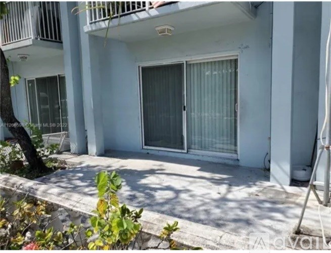 A white building with a balcony and a tree in front.