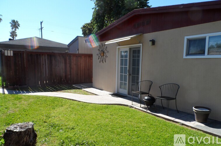 A house with a red roof and a white door is surrounded by a wooden fence and has a small garden in front.