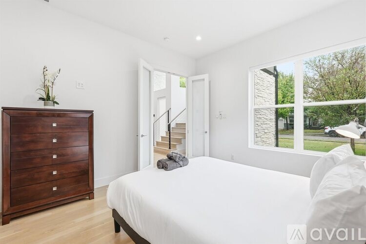 A bedroom with a large bed, a wooden dresser, and a window overlooking a lawn.
