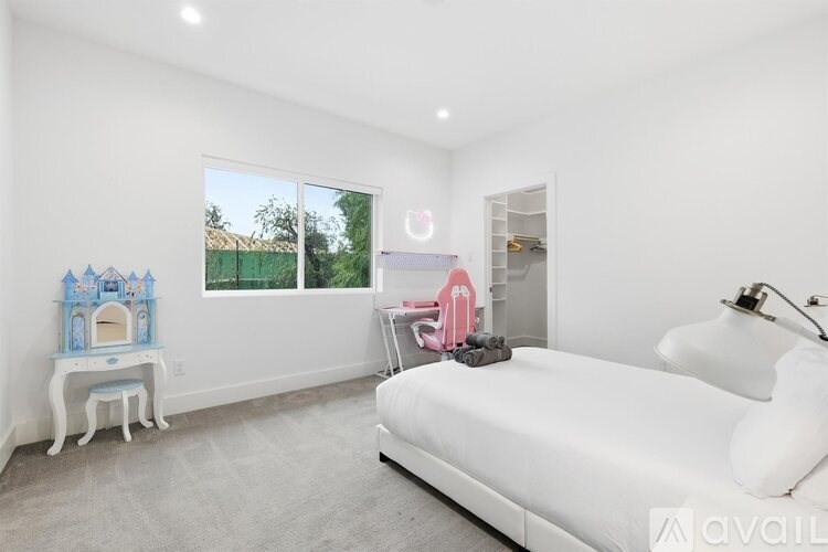 A white bedroom with a bed, chair, and a small table with a blue castle.