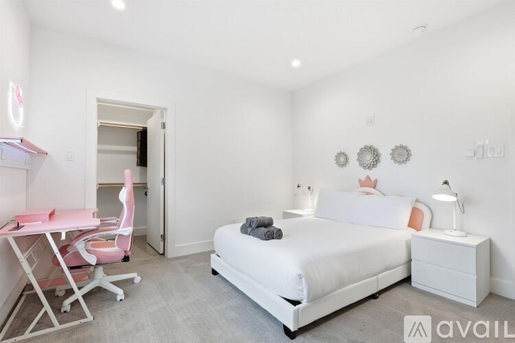 A bedroom with a white bed, a pink chair, and a white desk.