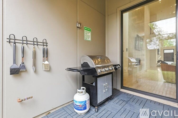 A grill is on a stand next to a wall with hooks for hanging tools.
