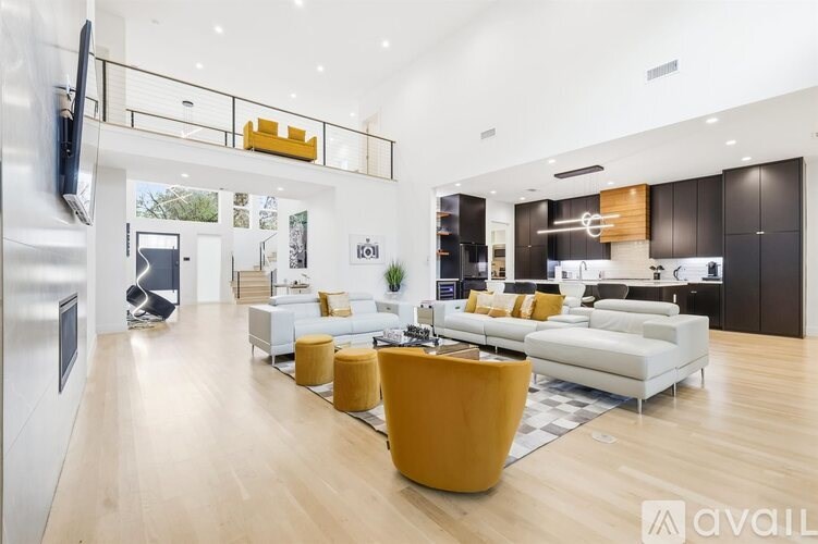 A modern living room with a white sofa set and yellow ottoman.