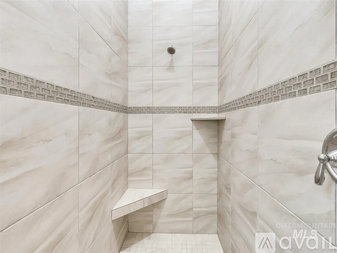 A white tiled bathroom with a bench and a shower head.