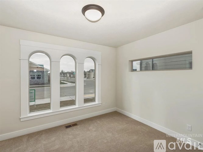 A room with a carpeted floor, a window with blinds, and a wall-mounted light fixture.