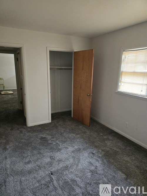 A room with a carpeted floor, a wooden door, and a window with blinds.