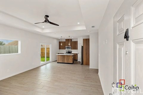 A spacious room with a ceiling fan and a kitchen area in the background.