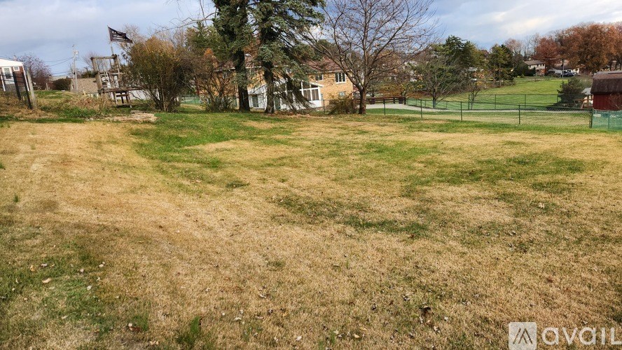 A grassy field with a fence and trees in the background.