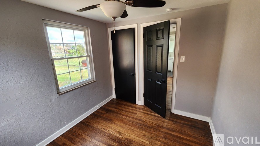 A room with a window, a ceiling fan, and a door.
