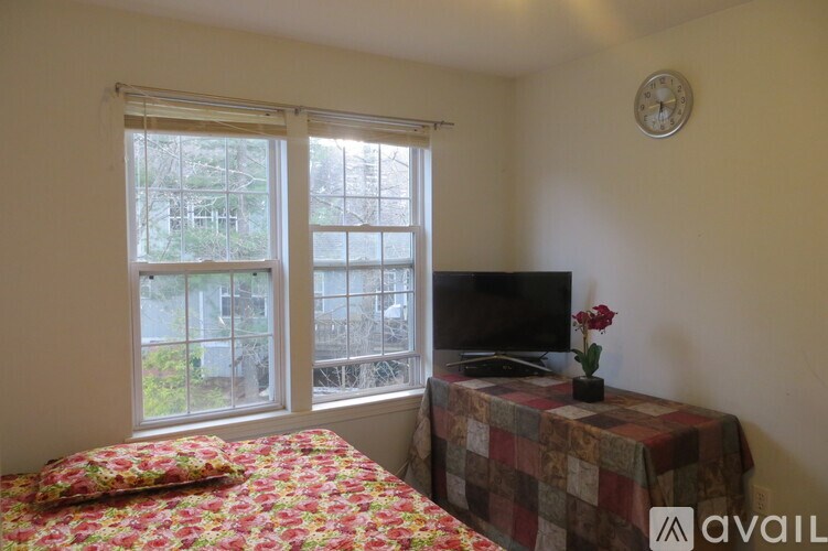 A bedroom with a bed, a table with a TV and a clock on the wall.
