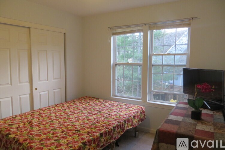 A bedroom with a floral bedspread and a window showing a view of a tree.