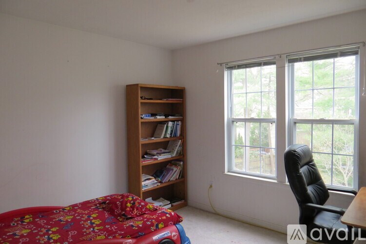 A room with a bookshelf, a window with a view of trees, and a bed with a floral comforter.