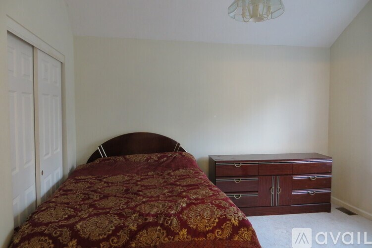 A bedroom with a bed, dresser, and chandelier.