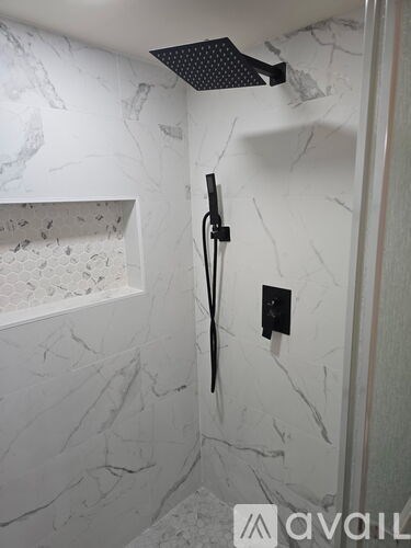 A shower with a black hose and a black handle.