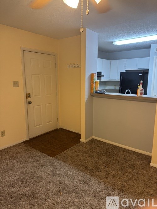 A room with a white door and a kitchen area with a black fridge.