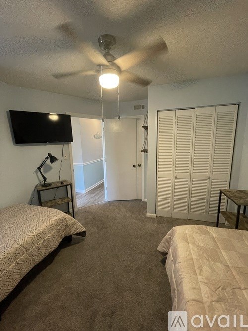A bedroom with a bed, a ceiling fan, and a television mounted on the wall.
