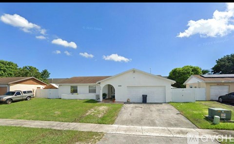 A white house with a garage is surrounded by a green lawn and a clear blue sky.