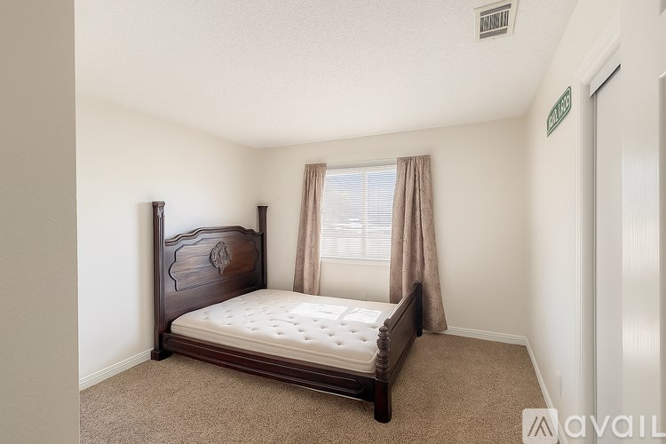 A bedroom with a bed, carpet, and a window with curtains.