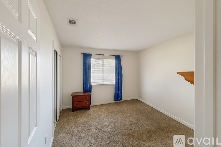 A room with a carpeted floor, a window with blue curtains, and a wooden staircase.