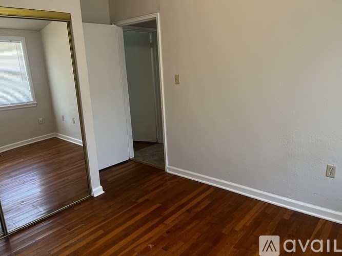 A room with wooden floors and a white wall with a doorway leading to another room.