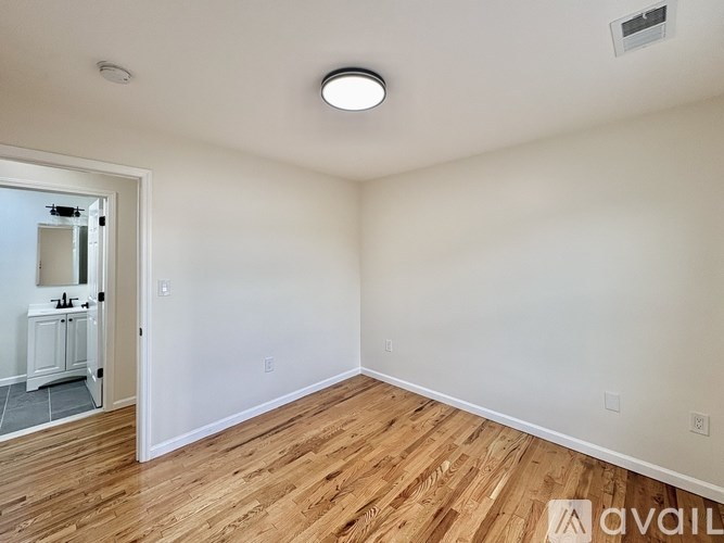 A room with wooden flooring and a white wall with a doorway leading to another room.