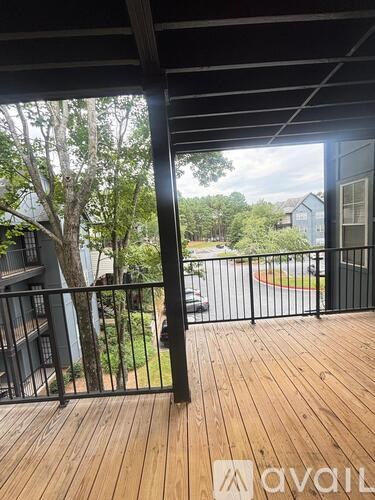 A balcony with a black railing and wooden floor overlooks a tree and a road.