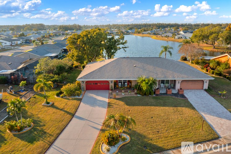 A house with a red garage door is surrounded by a well-kept lawn and a body of water in the distance.