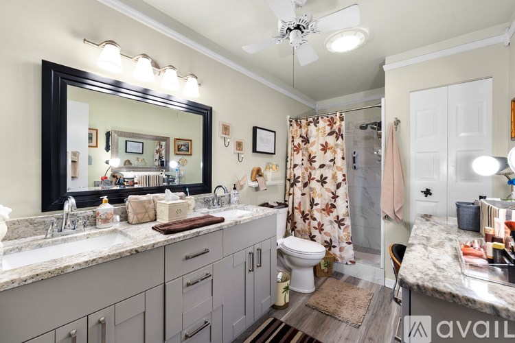 A bathroom with a large mirror, a sink with two faucets, a toilet, a shower curtain, and a rug on the floor.