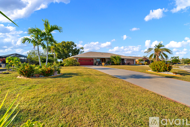 A house with a red roof is surrounded by greenery and palm trees.