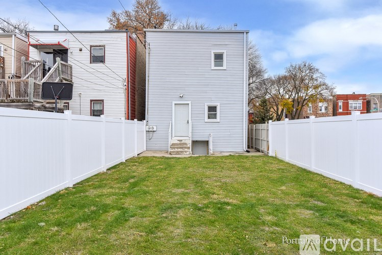 A backyard with a white fence and a grey house.