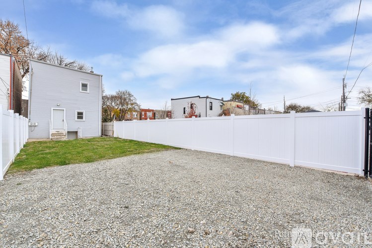 A gravel driveway leads to a white house with a white fence.